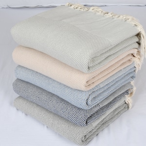 Puede incluir: Una pila de cinco toallas turcas en varios colores, incluyendo gris claro, beige y azul. Las toallas están dobladas y tienen una textura de gofre.