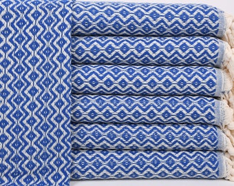 May include: A stack of blue and white patterned Turkish towels with fringe. The towels are folded and stacked on a white background.