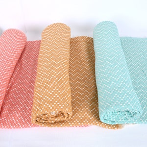 May include: Four rolled up throw blankets in different colors: coral, mustard yellow, tan, and light blue. Each blanket has a white chevron pattern and a fringe edge.