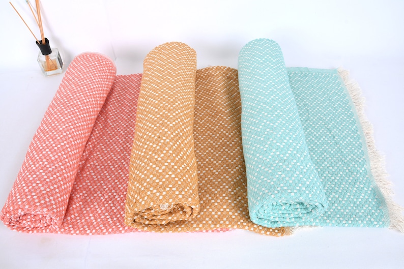 May include: Four rolled up throw blankets in different colors: coral, mustard yellow, tan, and light blue. Each blanket has a white chevron pattern and a fringe edge.