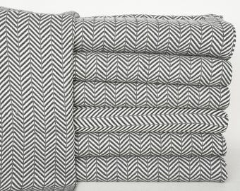 May include: A stack of gray and white herringbone patterned throw blankets. The blankets are folded and stacked on top of each other.