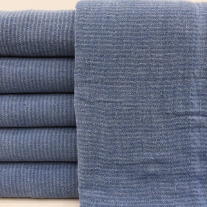 May include: A stack of six blue cotton towels, folded and arranged in a row. The towels have a textured, woven pattern.