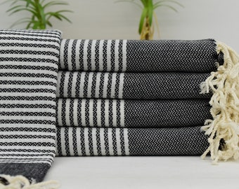 Puede incluir: Una pila de toallas turcas rayadas en blanco y negro con flecos blancos. Las toallas están dobladas y apiladas sobre una superficie blanca.