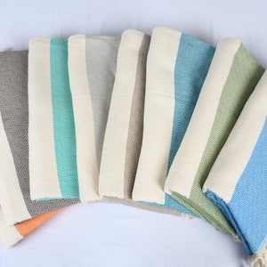 May include: A set of seven striped towels in various colors, including orange, gray, teal, beige, green, and blue. The towels are folded and arranged in a semi-circle.