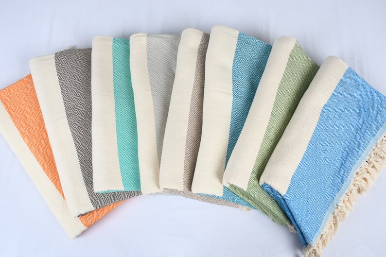 May include: A set of seven striped towels in various colors, including orange, gray, teal, beige, green, and blue. The towels are folded and arranged in a semi-circle.