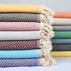Pode incluir: Uma pilha de mantas de algodão tecidas coloridas com franjas nas bordas. As mantas apresentam um padrão de losangos em várias cores, incluindo amarelo, rosa, verde, azul e roxo.