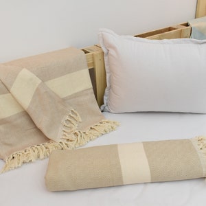 May include: Two beige and white striped throw blankets with fringe edges. One blanket is folded and the other is rolled up. The blankets are on a white bed with a white pillow.