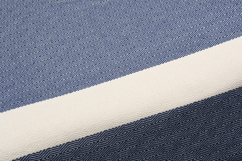 May include: A blue and white striped Turkish towel with a diamond pattern. The towel is made of cotton and is soft and absorbent.