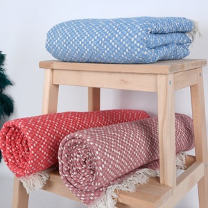 May include: Two rolled up blankets on a wooden stool. One blanket is a light blue with a white diamond pattern, and the other is a coral color with a white diamond pattern.