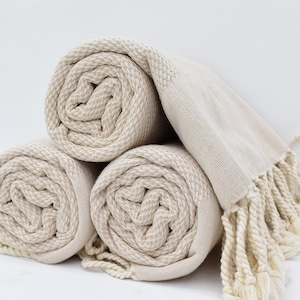 May include: Three rolled up beige towels with fringe. The towels are made of a soft, absorbent material and are perfect for drying off after a shower or bath.