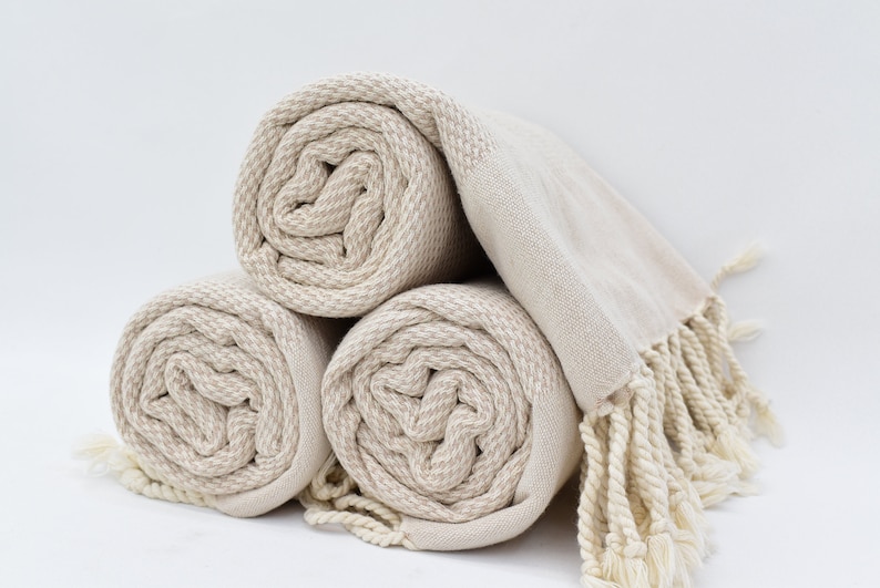 May include: Three rolled up beige towels with fringe. The towels are made of a soft, absorbent material and are perfect for drying off after a shower or bath.
