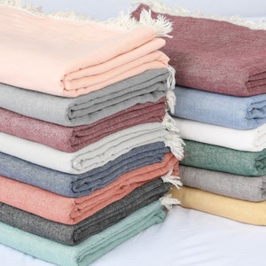 May include: A stack of 10 cotton throws in various colours, including light pink, grey, burgundy, light grey, navy blue, dark red, black, dark green, light green, and yellow.