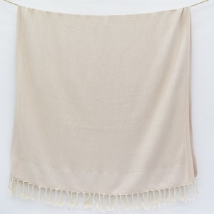 May include: A cream-coloured throw blanket with a fringe border. The blanket is made of a soft, textured fabric.