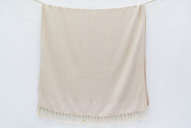 May include: A cream-coloured throw blanket with a fringe border. The blanket is made of a soft, textured fabric.