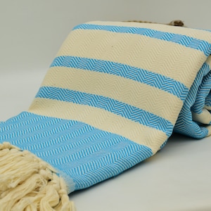 May include: A light blue and cream striped Turkish towel with fringe. The towel is rolled up and has a chevron pattern.