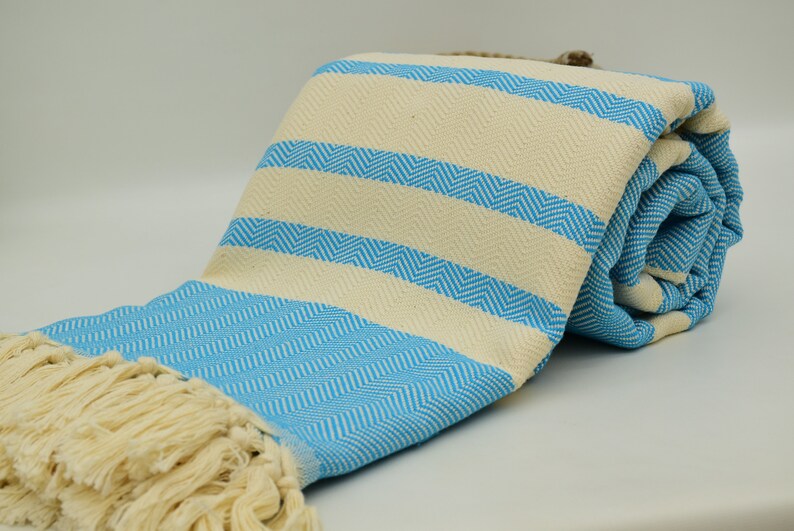 May include: A light blue and cream striped Turkish towel with fringe. The towel is rolled up and has a chevron pattern.