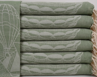 May include: A stack of six green Turkish towels with a white hot air balloon design. The towels have white fringe on the ends.