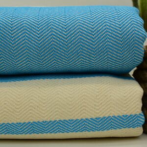May include: Two folded Turkish towels with a chevron pattern. The top towel is turquoise blue and white, and the bottom towel is white with a turquoise blue border.