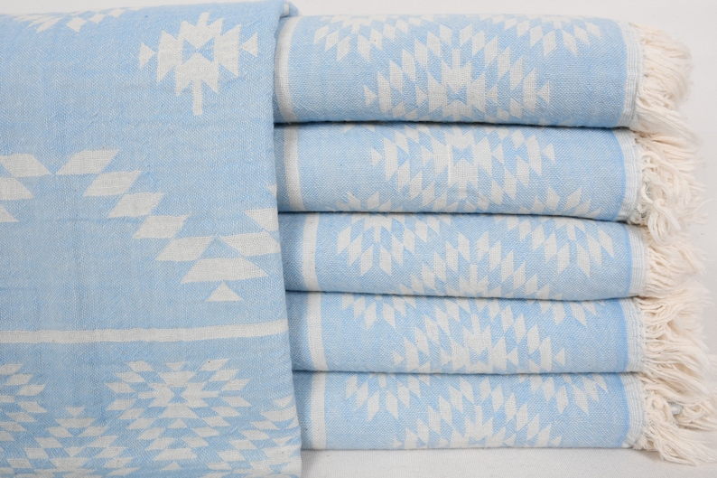 Pu&ograve; includere: Un mucchio di sei asciugamani di colore azzurro chiaro con un motivo geometrico bianco. Gli asciugamani hanno frange bianche alle estremit&agrave;.