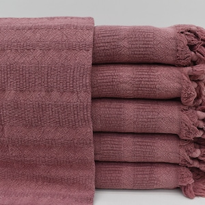 Puede incluir: Una pila de seis toallas rosas con bordes con flecos. Las toallas están hechas de un tejido suave y texturizado.