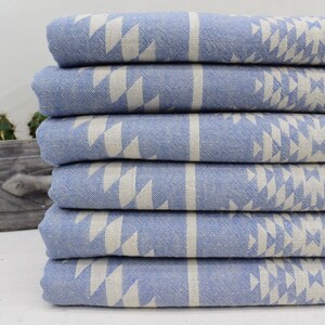 Peut inclure: Une pile de six serviettes de bain bleues et blanches &agrave; motifs. Les serviettes sont pli&eacute;es et empil&eacute;es les unes sur les autres. Les serviettes ont un motif g&eacute;om&eacute;trique de triangles blancs sur un fond bleu clair.