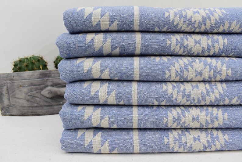 Peut inclure: Une pile de six serviettes de bain bleues et blanches &agrave; motifs. Les serviettes sont pli&eacute;es et empil&eacute;es les unes sur les autres. Les serviettes ont un motif g&eacute;om&eacute;trique de triangles blancs sur un fond bleu clair.