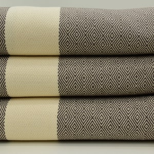 May include: A stack of three towels with a diamond pattern in brown and cream colors. The towels have fringe on the ends.