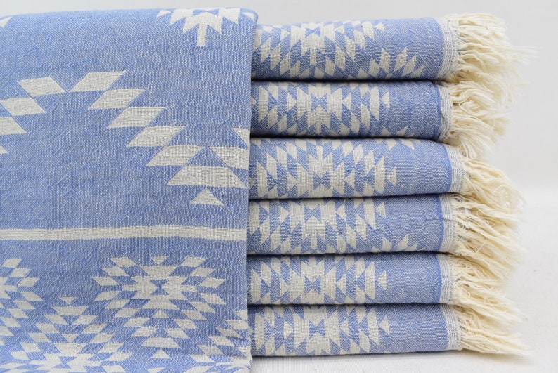 Peut inclure: Une pile de six serviettes turques bleu clair avec un motif g&eacute;om&eacute;trique blanc et des bords frang&eacute;s.