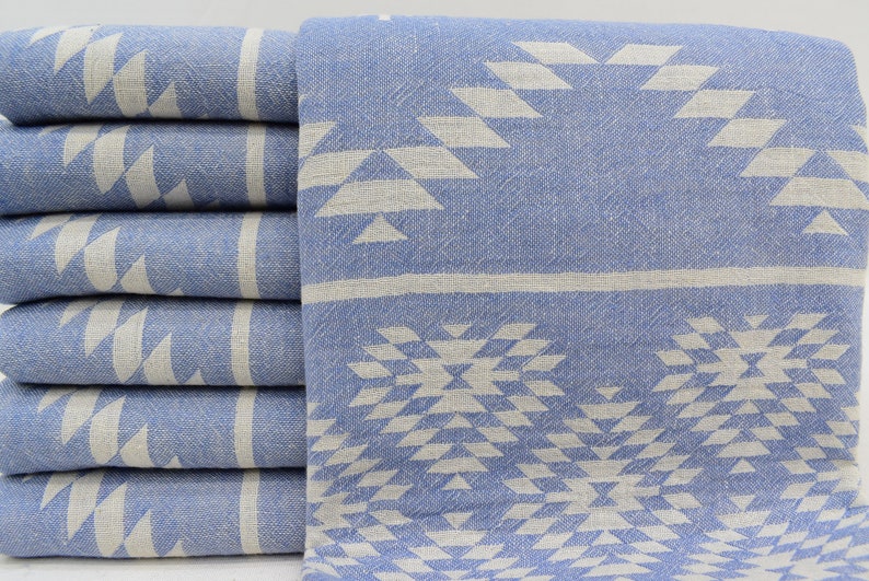 Peut inclure: Un lot de six serviettes turques &agrave; motifs bleus et blancs. Les serviettes pr&eacute;sentent un motif g&eacute;om&eacute;trique avec des triangles et des losanges blancs sur un fond bleu clair.