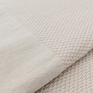 May include: A close-up of a beige woven fabric with a subtle pattern. The fabric is soft and textured, with a slightly rough feel.