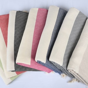 May include: A set of seven Turkish towels in various colors, including green, red, black, and blue. The towels are made of cotton and have a fringe on the ends. They are folded and arranged in a fan shape.