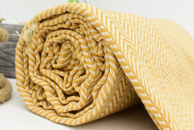 Op de afbeelding: Een gele en witte gestreepte deken met een herringbone-patroon. De deken is opgerold en de stof is zacht en textuur.