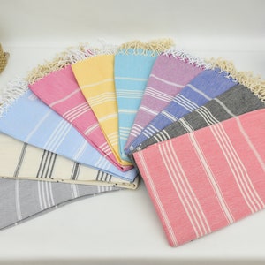 May include: A collection of ten striped towels in various colors, including pink, yellow, blue, gray, and white. The towels are arranged in a fan shape and have fringe edges.