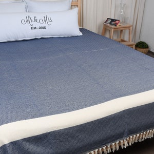 May include: A blue and white striped throw blanket with fringe on the edges. The blanket is on a bed with white pillows and a pillow with the text "Mr. & Mrs. Est. 2015".