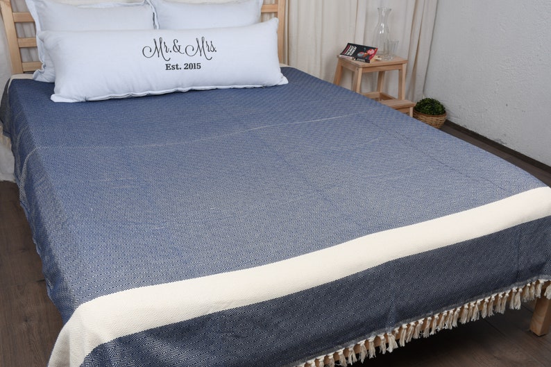 May include: A blue and white striped throw blanket with fringe on the edges. The blanket is on a bed with white pillows and a pillow with the text "Mr. & Mrs. Est. 2015".