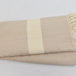 May include: A beige Turkish towel with a white stripe down the center and fringe on the edges.