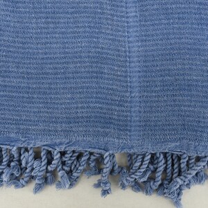 May include: A blue cotton throw blanket with a fringe border. The blanket has a woven texture.