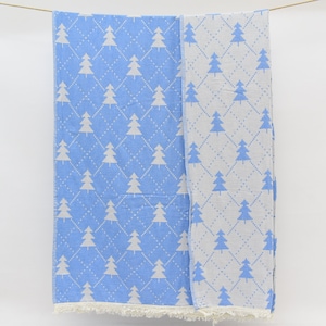 Op de afbeelding: Een blauwe en witte katoenen deken met een wit kerstboommotief. De deken heeft een franje rand.