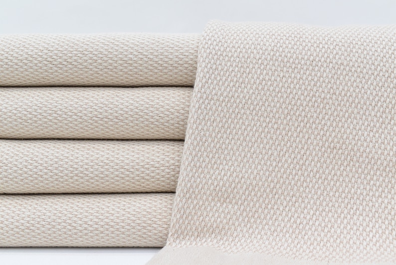 May include: A stack of four beige fabric towels with a textured weave. The towels are folded and stacked on a white surface.