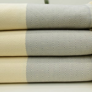 May include: A stack of three gray and cream striped towels with fringe. The towels have a diamond pattern.