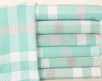 May include: A stack of six folded towels with a checkered pattern. The towels feature a repeating design of aqua, white, and gray squares. The pattern incorporates a zigzag texture within the squares, creating a textured appearance. The towels are neatly stacked.