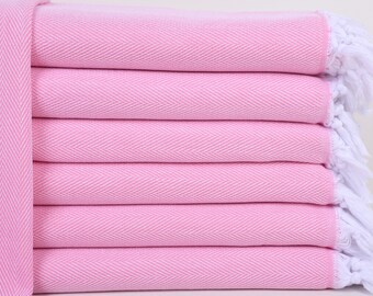Può includere: Un mucchio di asciugamani rosa con frange bianche. Gli asciugamani sono piegati e impilati uno sopra l'altro.