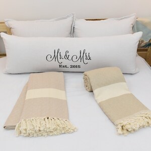 May include: Two beige and white striped throw blankets with fringe on a white bed with white pillows. One pillow has the text "Mr. & Mrs. Est. 2015" embroidered on it.