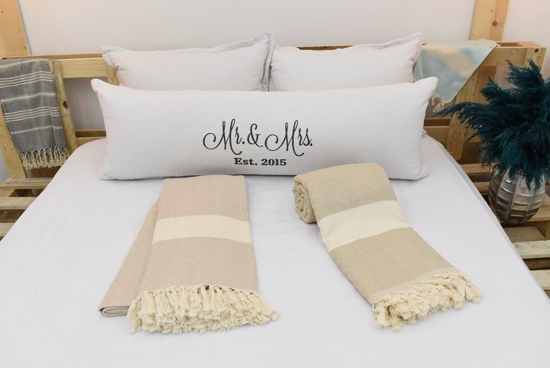 May include: Two beige and white striped throw blankets with fringe on a white bed with white pillows. One pillow has the text "Mr. & Mrs. Est. 2015" embroidered on it.