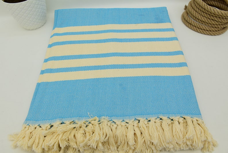 May include: A light blue and cream striped Turkish towel with a herringbone pattern and fringe.