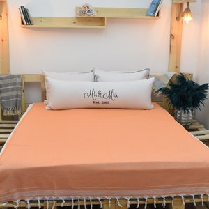 Puede incluir: Manteo de algodón turco de color melocotón con flecos blancos sobre un marco de cama de madera. La manta tiene una almohada blanca con el texto "Mr. & Mrs. Est. 2015" en ella.