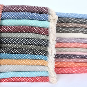 May include: A stack of 20 colorful woven throw blankets with fringe edges. The blankets are made of a soft, textured fabric and feature a variety of colors, including red, blue, green, and orange.