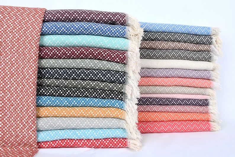 May include: A stack of 20 colorful woven throw blankets with fringe edges. The blankets are made of a soft, textured fabric and feature a variety of colors, including red, blue, green, and orange.
