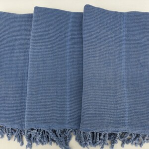 May include: Three blue cotton towels with fringe edges. The towels are folded and stacked on top of each other.