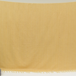 Op de afbeelding: Een gele deken met een herringbone patroon en franjes.